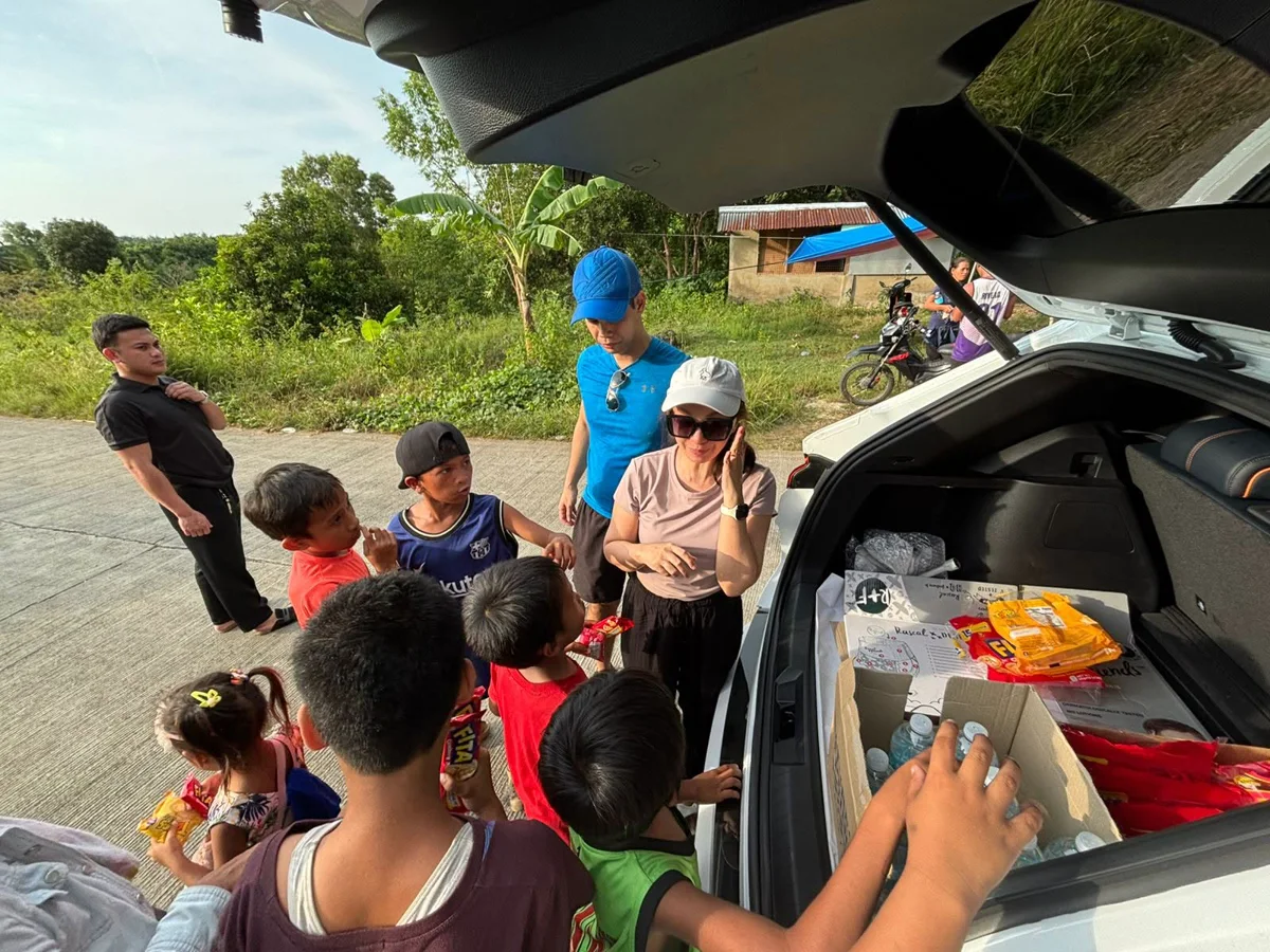 Children gathered at the open boot of a car being handed supplies